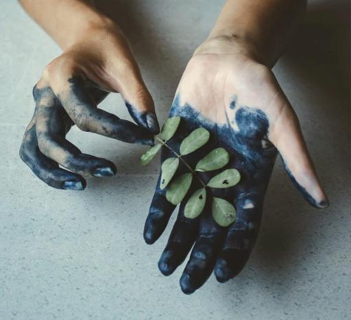 Hände sind schmutzig mit schwarz-blauer Farbe und halten ein grünes Blatt