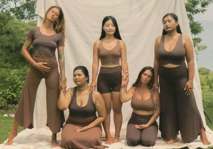 Fünf Frauen in braunen Yogahosen und Oberteilen machen gemeinsam ein Foto